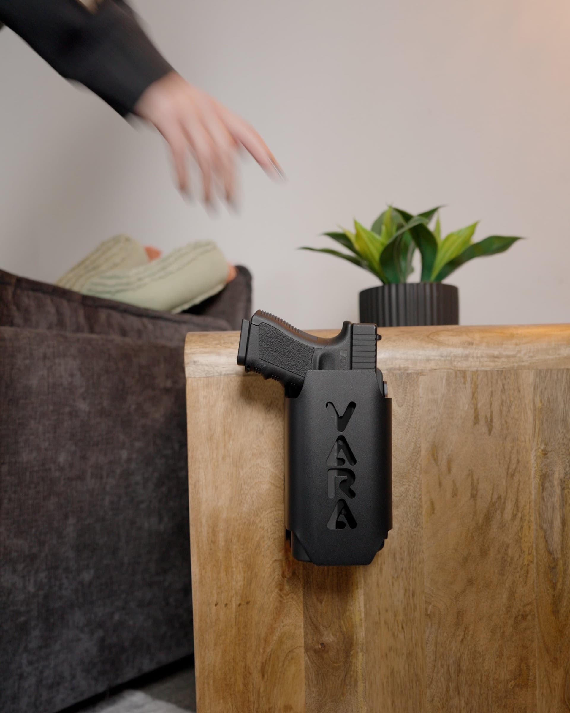 Reach Tactical mounted on the side of a wooden nightstand holding a pistol, a hand reaching for it