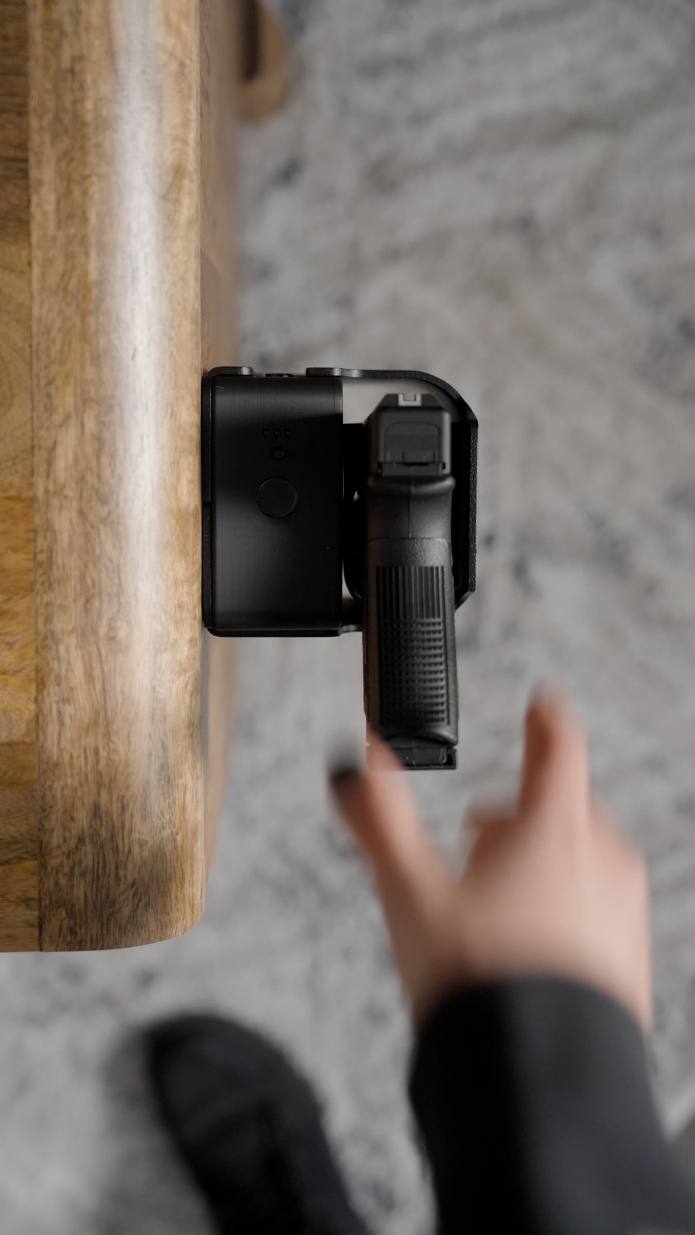 Seen from above, a hand reaching toward a pistol held in a Reach safe on the side of a nightstand