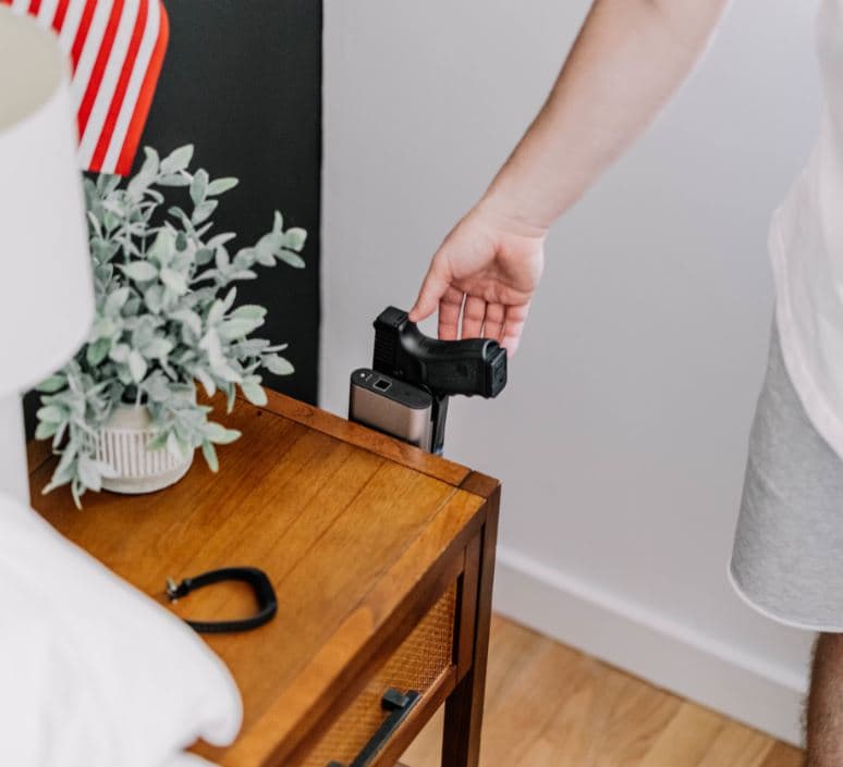 A hand drawing a pistol from a Reach mounted on a bedside table
